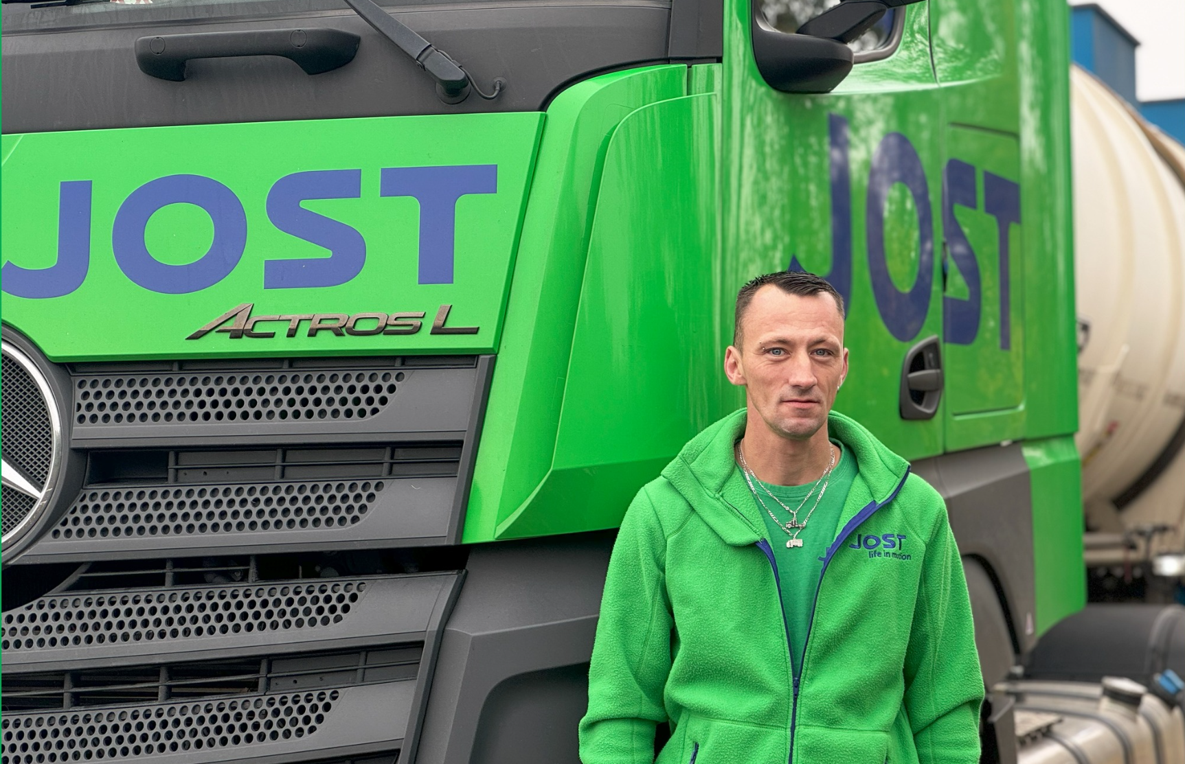 Un chauffeur debout devant un camion Mercedes vert arborant le logo JOST, prêt pour une nouvelle mission de transport.