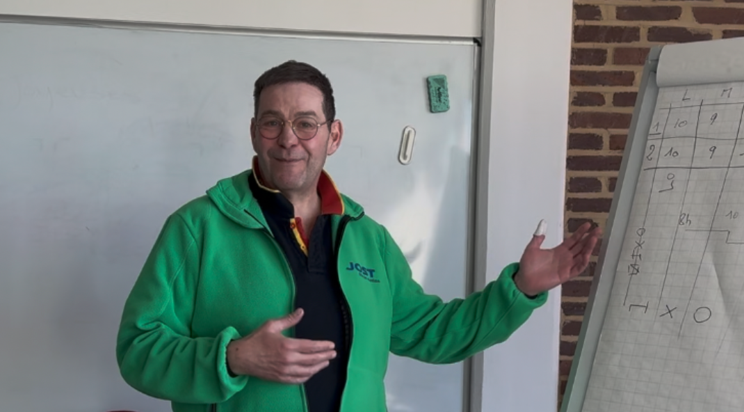 A man wearing a green JOST vest standing near a whiteboard