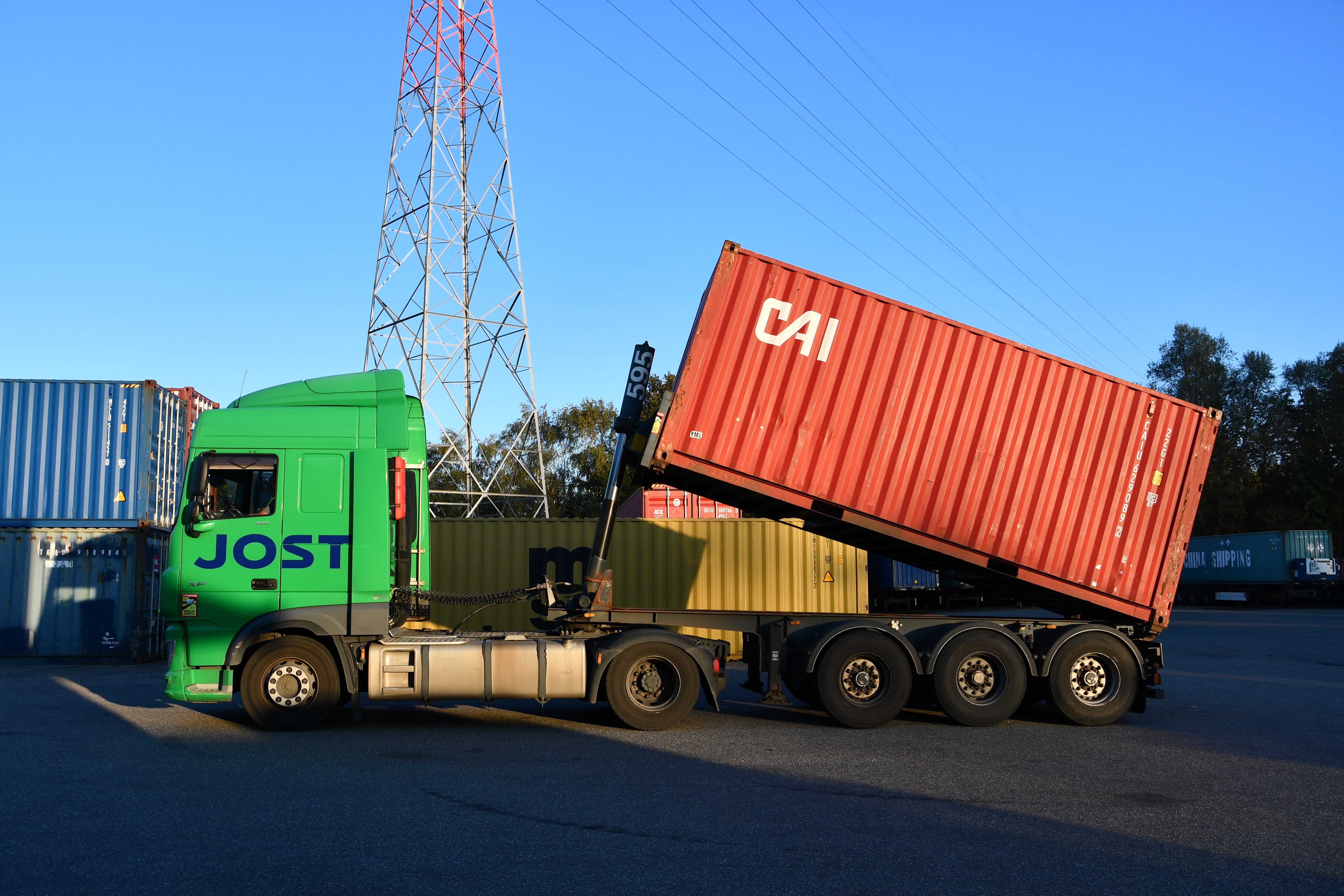 Camion JOST effectuant une manipulation en soulevant un conteneur de couleur rouge