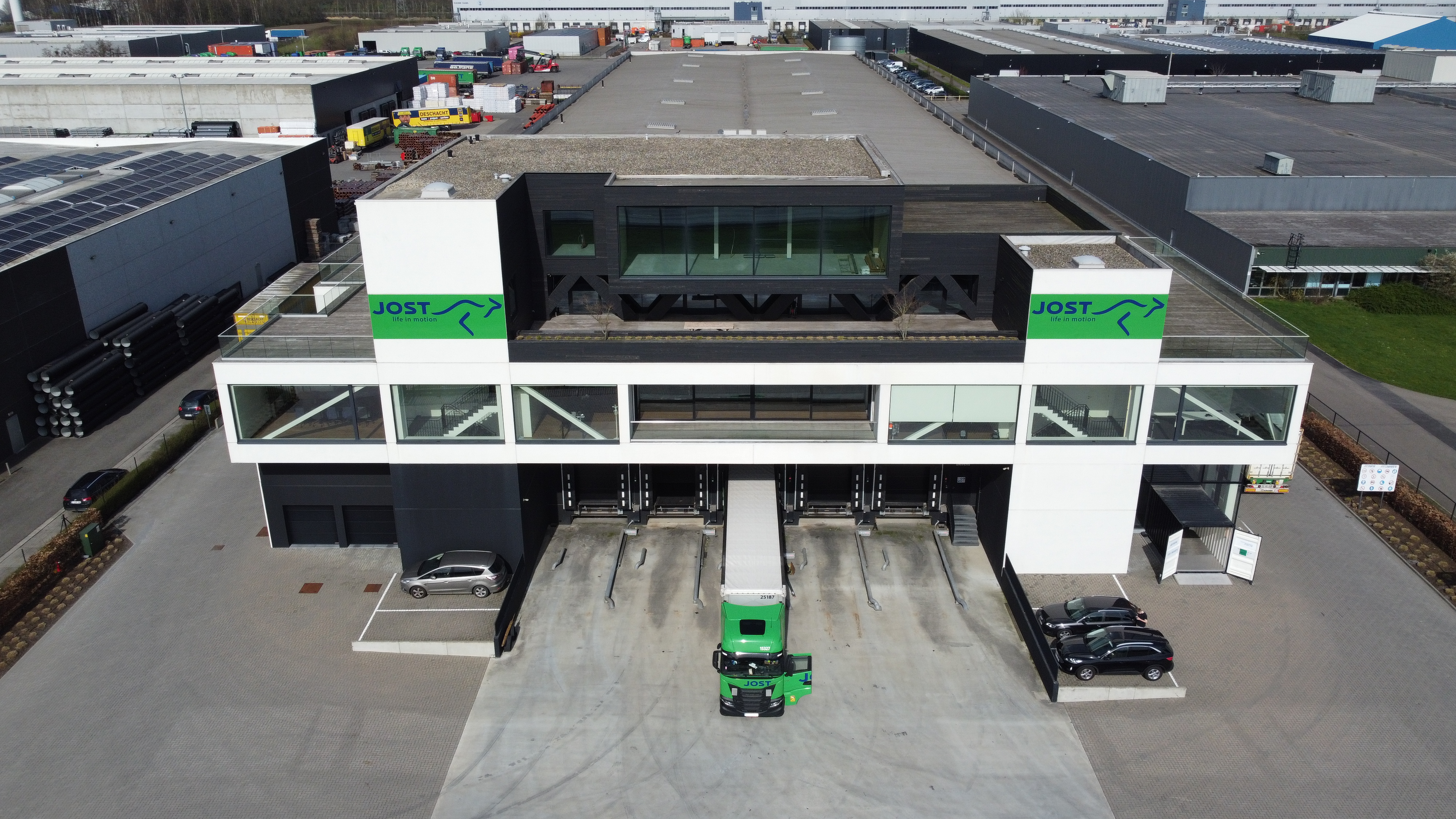 Site Jost à Geel vue en drone sur un bâtiment avec un camion de transport garé devant avec une porte ouverte.