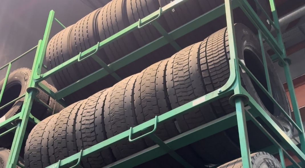 Gestapelde banden zijn netjes gerangschikt op groene stalen rekken in een magazijn. De scène straalt een gevoel van orde en industriële efficiëntie uit.